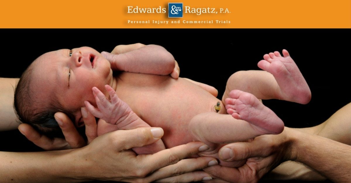 Newborn baby held safely in adult hands with Edwards & Ragatz, P.A. banner.
